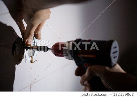 Close-Up of a Hand Using a Power Drill to Install a Wall Fixture Close-Up of a Hand Using a Power Drill to Install a Wall Fixture 122139068
