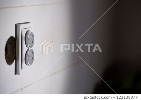 Close-up of a Wall Electrical Outlet with Surrounding Texture and Shadow Play Close-up of a Wall Electrical Outlet with Surrounding Texture and Shadow Play 122139077