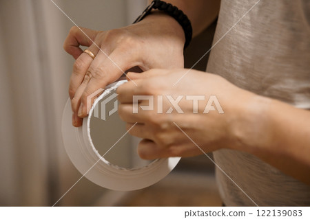 Close-Up of Hands Demonstrating a Crafting Technique with Tape Roll 122139083