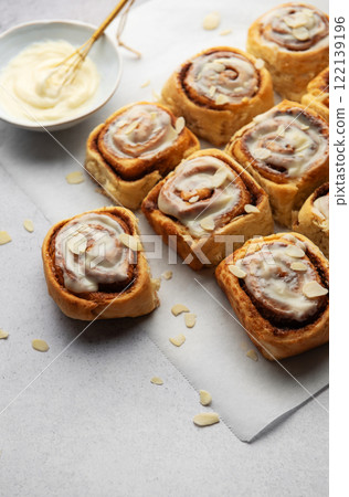Freshly baked cinnamon rolls topped with cream cheese frosting and almond slivers 122139196