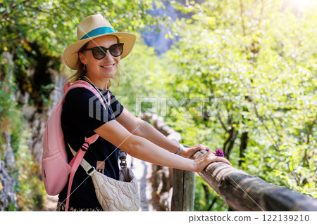 Portrait young adult woman female traveler wearing pink backpack straw hat enjoy hiking nature woods forest Plitvice Lakes National Park, Croatia. Tranquil green woods landscape trip trekking tour 122139210
