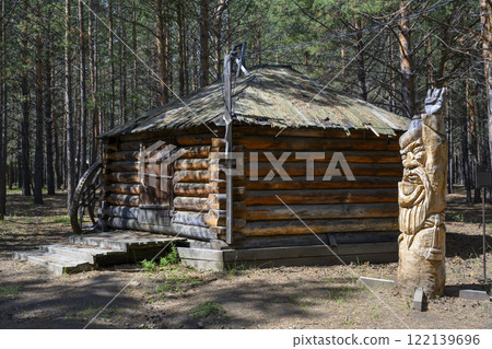 Sculpture of an elder of the Buryat family 'Serzhem' near a wooden barn in a pine forest 122139696
