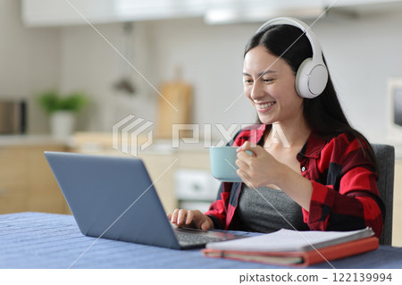 Happy asian student using headphone and laptop in the kitchen 122139994