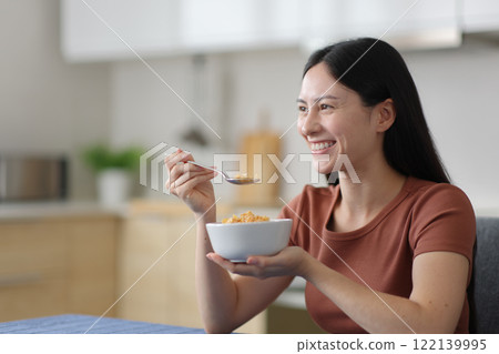 Happy asian woman eating cereals in a kitchen 122139995