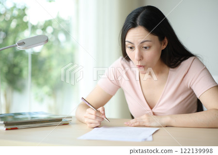 Amazed asian woman reading contract ready to sign at home Amazed asian woman reading contract ready to sign at home 122139998