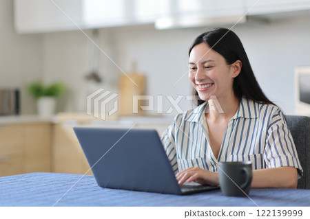 Happy asian woman using laptop in the kitchen Happy asian woman using laptop in the kitchen 122139999