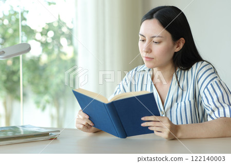 Serious asian woman reading a paper book on a desk 122140003