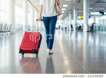 A woman walking through the airport with a red suitcase A woman walking through the airport with a red suitcase 122140265