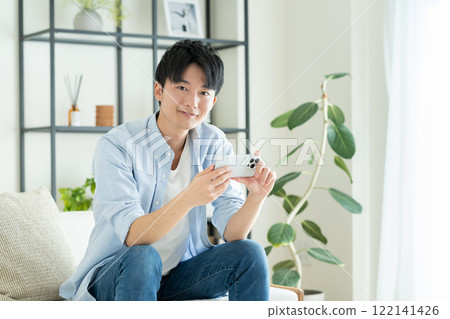 A young man looking at his smartphone in the living room A young man looking at his smartphone in the living room 122141426