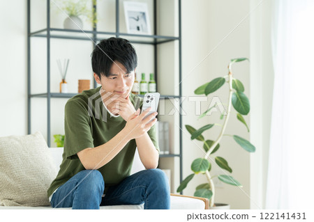 A young man looking at his smartphone in the living room 122141431