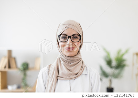 Portrait of a young Muslim woman doctor wearing hijab and glasses, exuding confidence and professionalism. Represents diversity, healthcare, and empowerment in medical field. Portrait of a young Muslim woman doctor wearing hijab and glasses, exuding confidence and professionalism. Represents diversity, healthcare, and empowerment in medical field. 122141765