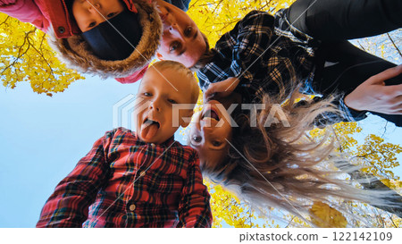 Cheerful family laughing, playing amid vibrant autumn foliage, creating joyful memories in sunlit park setting Cheerful family laughing, playing amid vibrant autumn foliage, creating joyful memories in sunlit park setting 122142109