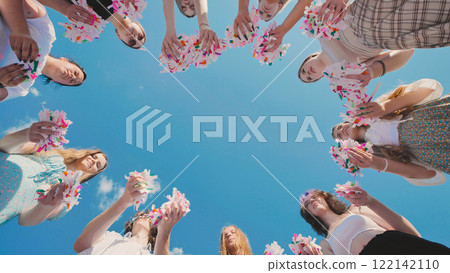 High school students in a circle, holding bright confetti against a vivid summer sky 122142110