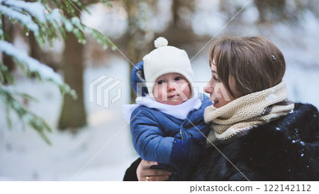 Mother holding her baby in a snowy forest during a winter day, enjoying a moment of family love and happiness Mother holding her baby in a snowy forest during a winter day, enjoying a moment of family love and happiness 122142112