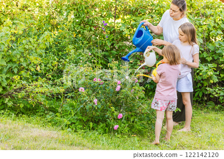 Family gardening activity with mother and daughters watering flowers 122142120