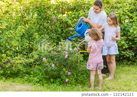Mother and daughters watering plants together in a summer garden 122142121