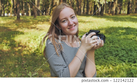 Young photographer smiling and holding a camera in a park, enjoying her passion for photography 122142122