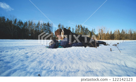 Mother and her son are lying on a snow covered field, cuddling and having fun on a beautiful winter day 122142123