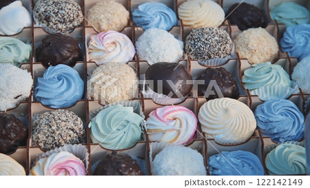 Colorful chocolate marshmallows and brownies at the bottom of the cookout. A woman with gloves is smoothing marshmallows. 122142149