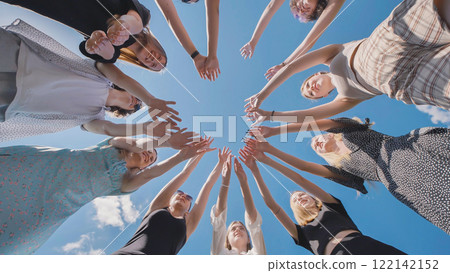 High school students joining hands in a circle, symbolizing teamwork and solidarity under a clear summer sky High school students joining hands in a circle, symbolizing teamwork and solidarity under a clear summer sky 122142152