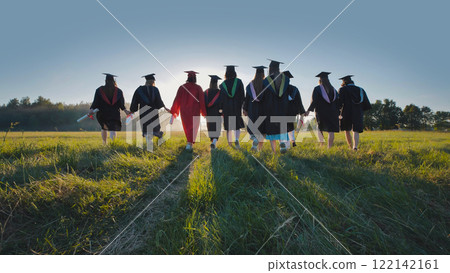Group of graduating students walking hand in hand through a sunlit field at sunset, celebrating their achievements and embracing new beginnings Group of graduating students walking hand in hand through a sunlit field at sunset, celebrating their achievements and embracing new beginnings 122142161