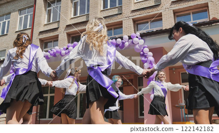 Female graduates in purple sashes celebrating their last day of school by dancing in a circle in front of their school Female graduates in purple sashes celebrating their last day of school by dancing in a circle in front of their school 122142182