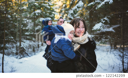 Happy family enjoying a sunny winter walk through a snowy forest, creating joyful memories while bonding together in nature's beauty 122142209