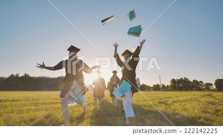 Group of elated graduates joyfully tossing their graduation caps in the air while celebrating their academic success in a field Group of elated graduates joyfully tossing their graduation caps in the air while celebrating their academic success in a field 122142225