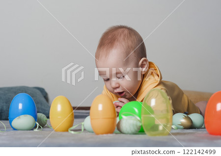 Baby in Yellow Outfit Playing with Colorful Easter Eggs on a Soft Carpet 122142499