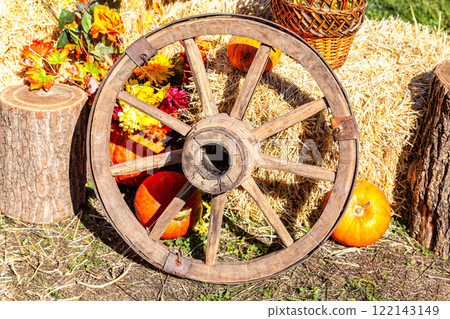 Autumn composicion with old wooden cartwheel, straw and pumpkins in sunny 122143149