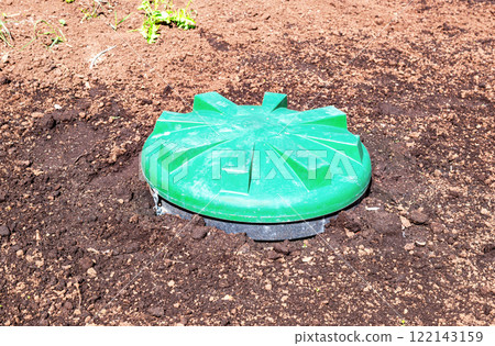 Covered sewer manhole of rural septic tank with green plastic cover, sewage system. Sewerage networks for country houses 122143159