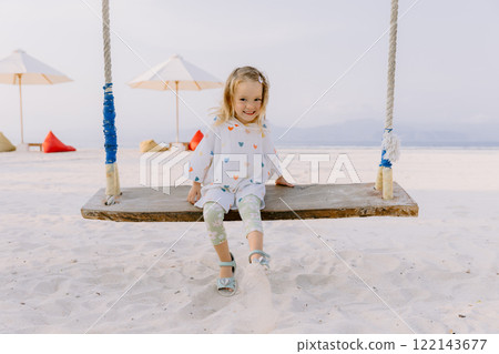 Little child girl plays and swinging on swings on beach, enjoy childhood 122143677