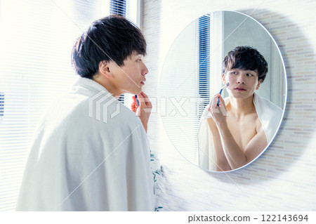 A young man shaving his beard 122143694