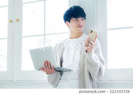 一個年輕人在窗邊用電腦工作 122143726