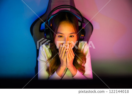 Asian happy Gamer endeavor plays online video games tournament with computer neon light, Smile young woman wearing gaming headphones intend to do playing live stream games online at home, font view Asian happy Gamer endeavor plays online video games tournament with computer neon light, Smile young woman wearing gaming headphones intend to do playing live stream games online at home, font view 122144018