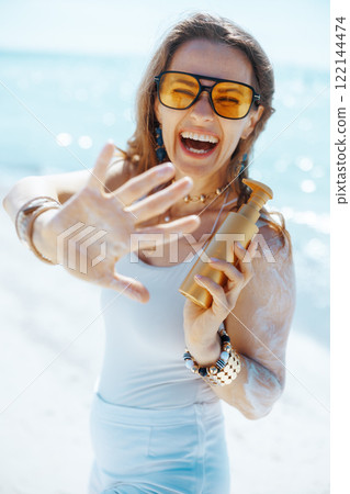smiling stylish woman on seashore with spf 122144474