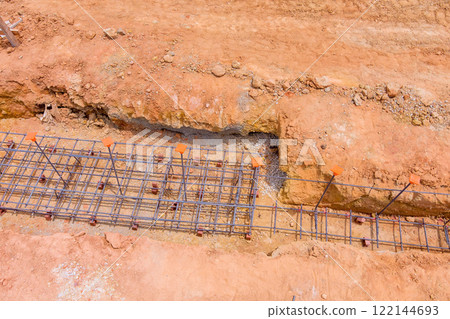 Construction work in progress with rebar grid laid in trench at site, showcasing groundwork for upcoming structure. 122144693