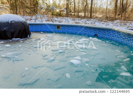 Ice covers surface of swimming pool, reflecting cold winter temperatures in forested setting. 122144695