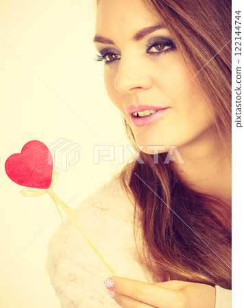 Flirty woman holding red wooden heart on stick Flirty woman holding red wooden heart on stick 122144744
