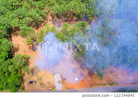 Smoke billows into air from a wooded area with construction equipment vehicles present in forest. 122144845