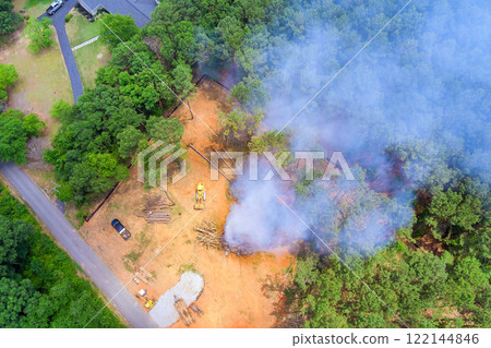 Controlled burn creates smoke as land clearing occurs in forested area, surrounded by trees, equipment. Controlled burn creates smoke as land clearing occurs in forested area, surrounded by trees, equipment. 122144846