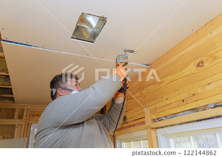 Worker is cutting drywall to fit fixtures while renovating wooden cabin, ensuring precise installation. 122144862