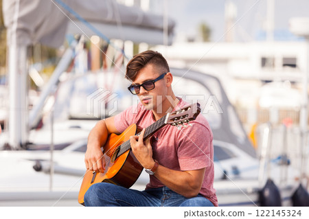 Young guitarist sitting on pier. Young guitarist sitting on pier. 122145324