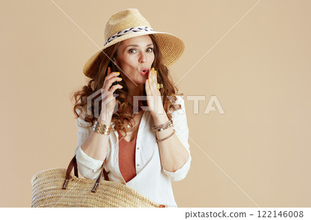 surprised woman in blouse and shorts talking on phone on beige 122146008