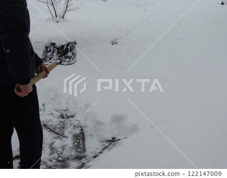 part of a figure of a man in dark clothes with a raised shovel against a background of clean fresh snow cover, an abstraction symbolizing the readiness to remove the snow that has fallen heavily 122147009