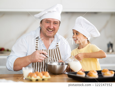 Father and daughter preparing muffins in kitchen Father and daughter preparing muffins in kitchen 122147352