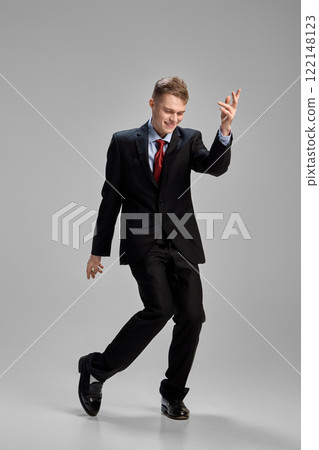 Joyful and happy young man, dressed formal attire dancing against grey studio background. Success and career growth. Joyful and happy young man, dressed formal attire dancing against grey studio background. Success and career growth. 122148123