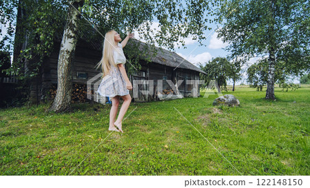 Barefoot woman stretching toward wooden barn branch, long blond hair flowing under summer sunlight Barefoot woman stretching toward wooden barn branch, long blond hair flowing under summer sunlight 122148150