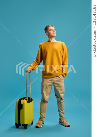 Full length photo of young man, dressed casually stands ready to adventures with luggage against blue studio background. 122148168