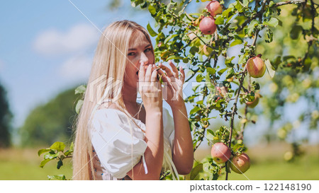 Blonde woman enjoying a fresh, ripe apple picked from a tree in an orchard, embracing nature's bounty Blonde woman enjoying a fresh, ripe apple picked from a tree in an orchard, embracing nature's bounty 122148190